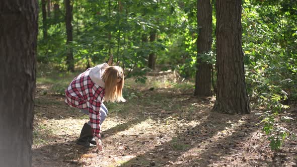 Live Camera Follows Young Woman Walking in Sunshine in Forest Gathering Branches for Bonfire alt
