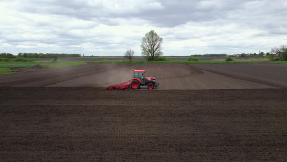 Slow Motion Aerial Shot of Tractor Plowing a Small Field with Blowing Dust in the Countryside of a alt