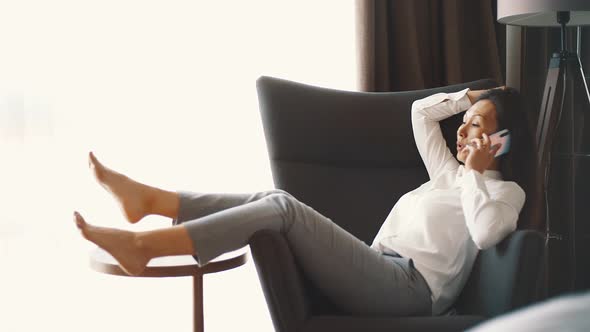Businesswoman lying on armchair in a hotel having phone call