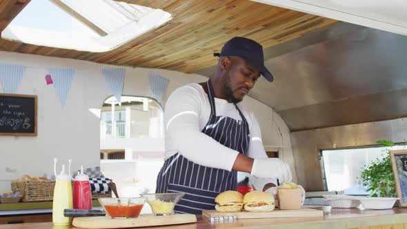 Portrait of african american man wearing apron smiling while preparing burgers in the food truck alt