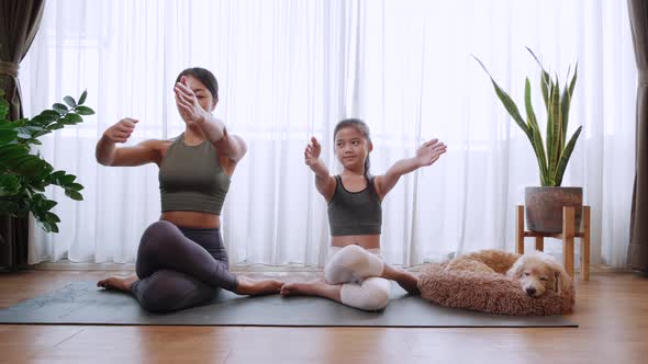 Happy Asian mother and daughter doing yoga sitting on yoga mat at home together