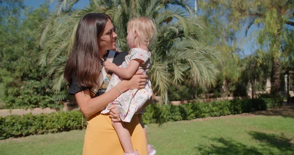 Beautiful Mother and Cute Little Daughter Talking in a Green Tropical Park alt