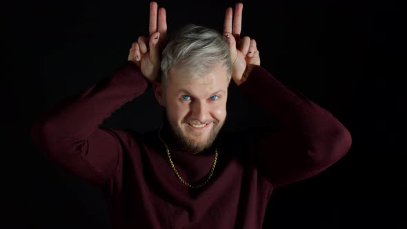 Funny Joyful Man in Stylish Blouse Making Bunny Ears Hand Gesture Over Head on Black Background alt