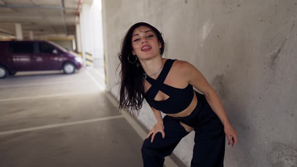 Dancing Sexy Woman Performs Modern Dance Posing Twerking in Parking Zone Leaning on Wall alt