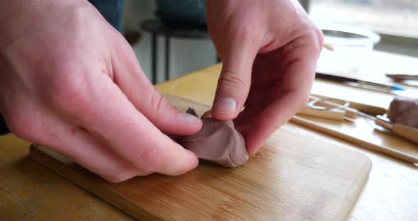 An artist pulling and stretching a piece of soft brown modeling clay and then sculpting with it on a alt