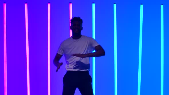 Flexible African American Man Dancing in the Studio Against the Backdrop of Multicolored Neon Lights alt