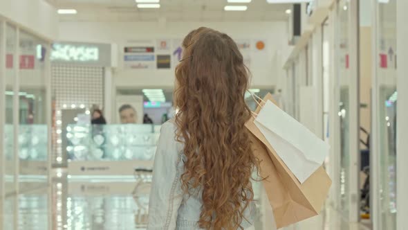Rear View Shot of a Curly Haired Little Girl Looking at Clothing Stores at Shopping Mall alt