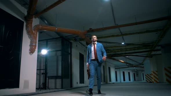 Businessman in a jacket walks through an underground parking lot home with a suitcase