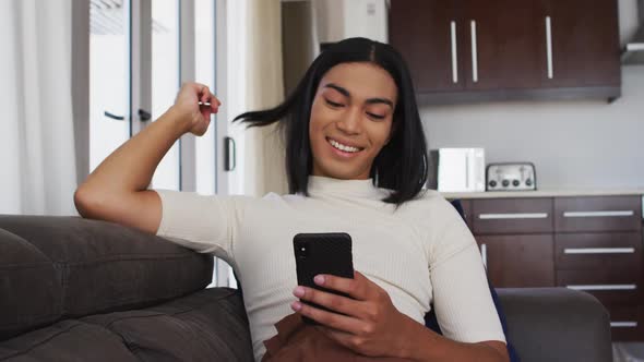 Gender fluid male smiling while using smartphone sitting on the couch at home alt