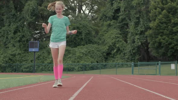 Cute young girl teenager walks on track twirling her headphones in slow motion. alt