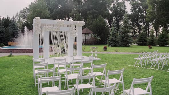 Beautiful wedding arch in the park with white chairs alt