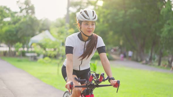 Asian young sport woman exercise by cycling riding bicycle workout in the evening in public park. alt