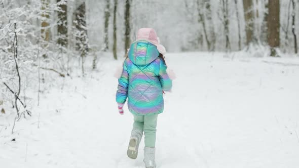 Cute Child Girl in a Colorful Clothing and Hat Running in Snowy Winter Park