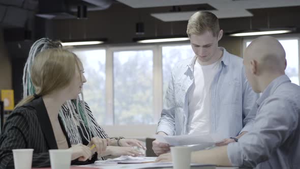 Group of Positive Young Caucasian Coworkers Talking and Laughing Sitting in Office alt