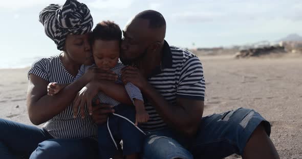 Happy african parents having tender moment on the beach with little son alt