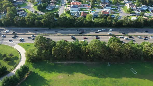 An aerial view of a parkway in the evening at rush hour. The camera truck left over a nearby park wh alt