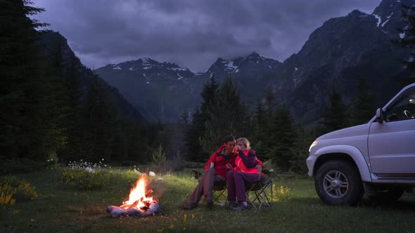 Time-lapse of Couple Chatting By Bonfire in Camping in Mountain Valley. Sunset 