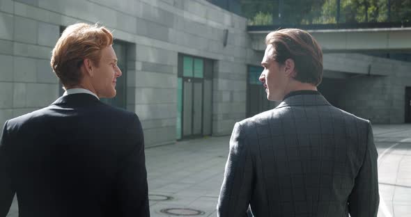 Back View of Two Businessmen Discussing Deals While Walking Outside Office at Break alt