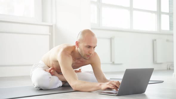 Young Bald Man Going to Perform Complex Yoga Pose Through Online Instructions
