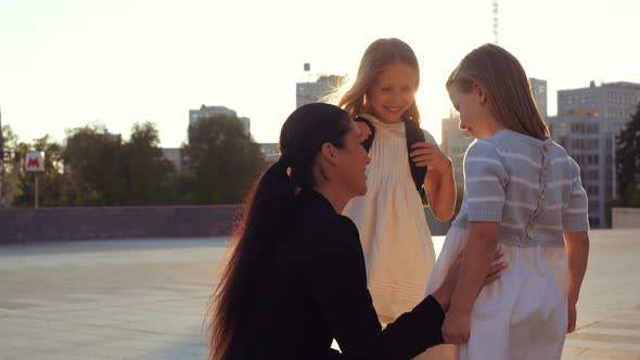 Close Up Good Looking Brunette Mum Woman Parent Embracing Two Little Kid Sisters Pupil on Schoolyard alt