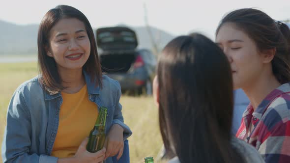 Group of a young Asian woman happy with friends camping in nature having fun together drinking beer.