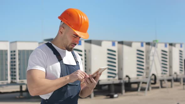 A Serious Young Engineer is Working on the Tablet and Looking at the Camera alt