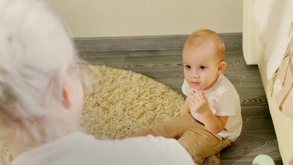 Cute Baby Boy Sitting on Floor and Listening to Grandma