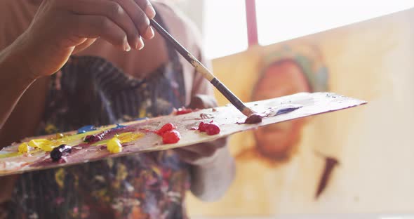 Mid section of male artist wearing apron mixing colors in a palette with a brush at art studio alt