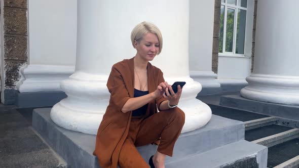Young Blonde Business Lady Reads a Message on a Smartphone and Rejoices