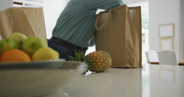Happy african american plus size woman unpacking shopping bags in kitchen alt