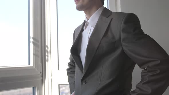 Young Successful Businessman Standing in Front of Windows Looking Into Distance on the City