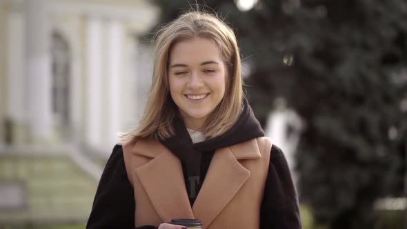 Portrait of Smiling Young Woman Having Leisure Standing Against Beautiful Building Holding Takeaway alt