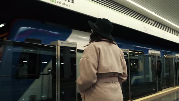 Rear View of a Young Girl in a Hat Standing Next to a Passing Subway Waiting for a Ride alt