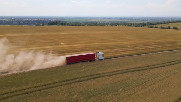 Aerial View of Lorry Cargo Truck Driving on Dirt Road Between Agricultural Wheat Fields alt