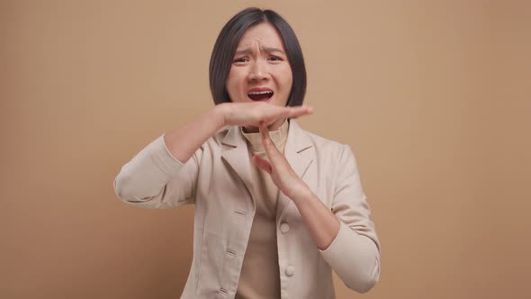 Asian business woman worried making a timeout gesture and standing isolated over beige background.