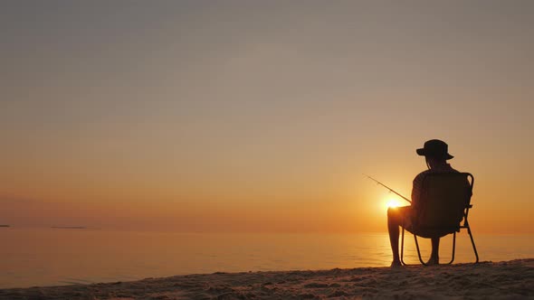 Silhouette of a Man Sitting By the Sea and Fishing. alt