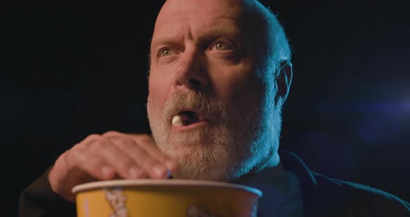 Focused senior man eating popcorn and watching a suspense movie at the cinema