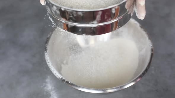 Сhef sprinkles flour in the bowl, using a sieve