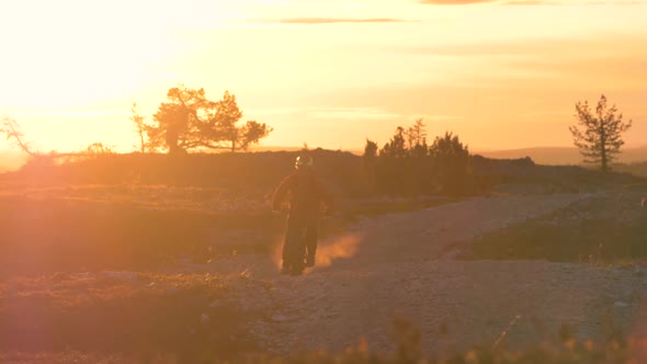 Young male fatbiking in Lapland with an electric fatbike and beautiful midnight sun behind him. alt