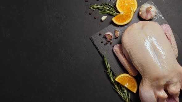 Raw Organic Whole Duck with Cut Orange and Rosemary on Slate Board on Black Background alt