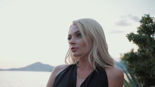Beautiful  blonde woman  in black dress walking at sunset against the sea alt