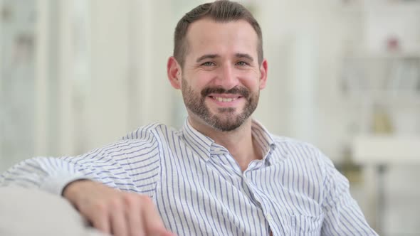 Young Man Sitting on Sofa and Smiling at Camera  alt
