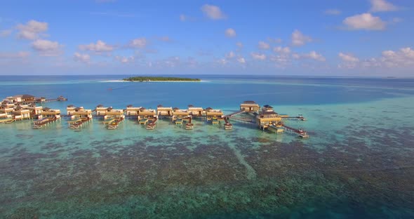 Aerial view of a couple lounging on an overwater bungalow at a tropical island resort hotel. alt