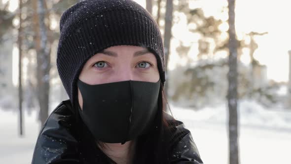 Portrait of a Young Woman in a Black Mask Stands in the City in the Winter alt