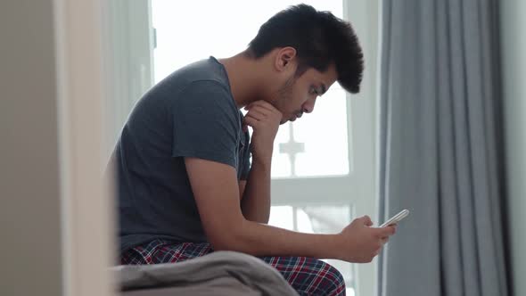 Pensive Indian man wearing t-shirt looking at the phone alt