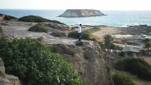 Extreme Wide Shot of African American Male Tourist Stretching Hands Standing on Cliffs on Blue alt