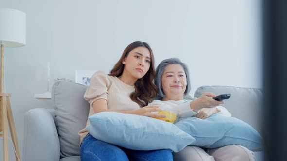 Asian senior mature woman and daughter sitting on sofa watching TV movie feel bored and stress. alt