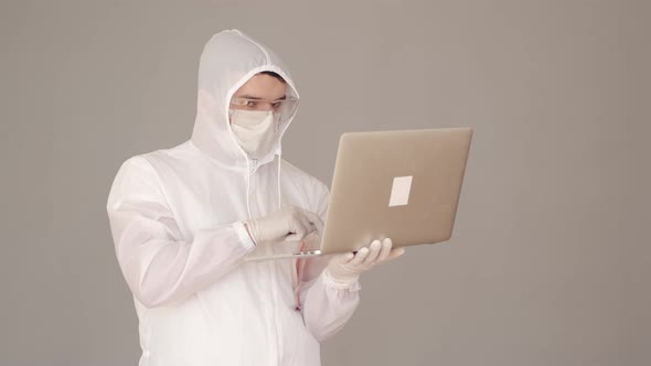 Man Scientist in a Full-covering Equipment Is Doing Research on Laptop alt