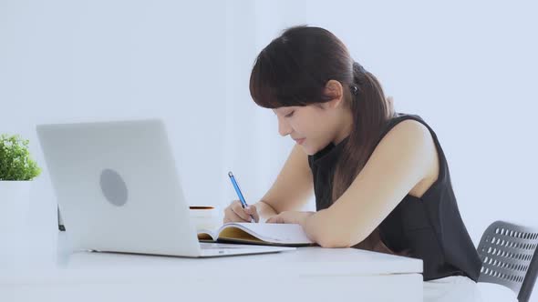 Beautiful asian woman smiling sitting in the living room study and learning writing notebook. alt