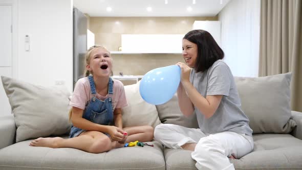 Mother and Teenage Daughter Having Fun Blowing Balloons Sitting on Couch in Living Room Slow Motion